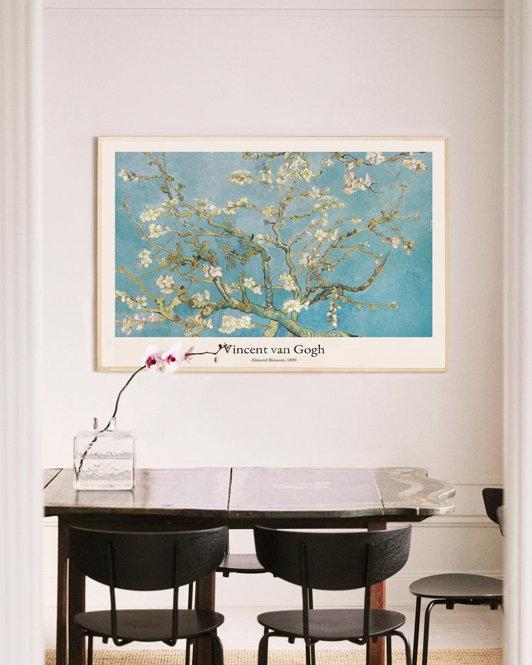 A dining area includes a wooden table and black chairs with a glass vase holding an orchid. An Almond Blossom by Vincent van Gogh poster is framed on a light wall, bringing elegance to the space.