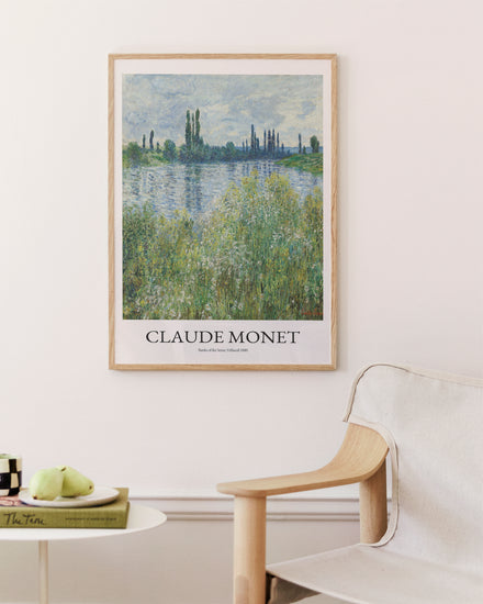 A Banks of the Seine by Claude Monet poster graces a white wall above a wooden chair. A side table with books and a bowl of green apples complements the serene, inviting setting.
