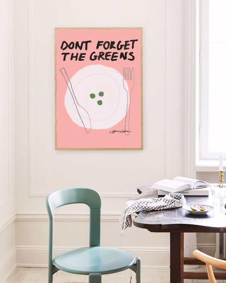 In a minimalistic dining room, a turquoise chair stands next to a dark wooden table. A humorous poster titled Dont Forget the Greens on the wall, with its pink backdrop and quirky cutlery and peas illustration, adds charm and whimsy to the tasteful decor.