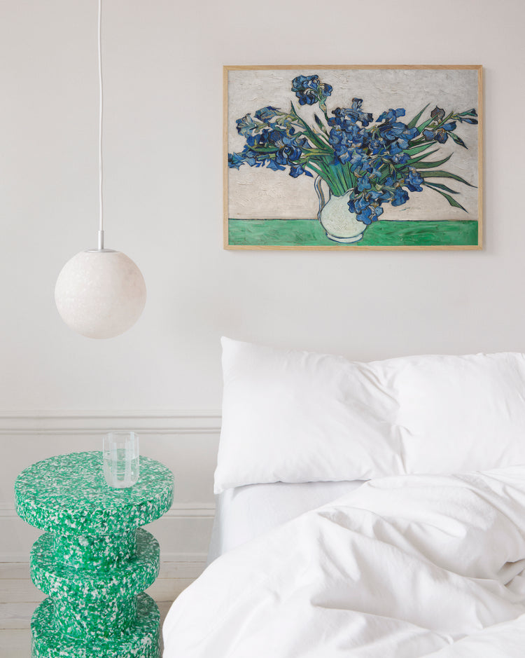 Framed artwork of Van Gogh's 'Irises' above a bed with a green side table.