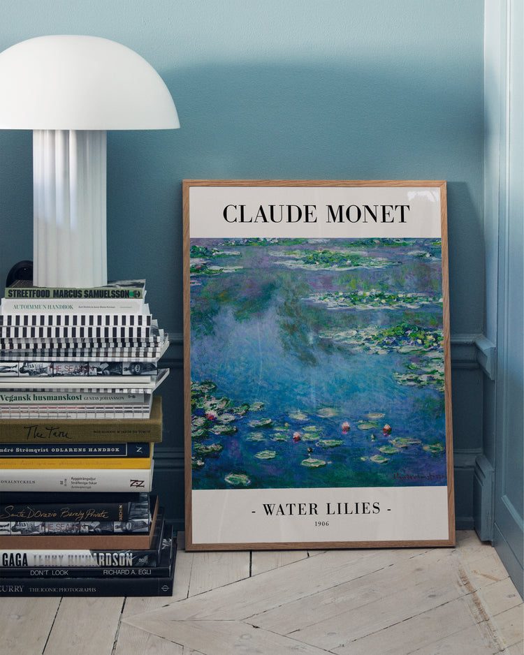 The Water Lilies by Claude Monet 1906 Poster leans against a teal wall next to a stack of books, with a white table lamp partially visible on the left, highlighting the famous Impressionist artwork.
