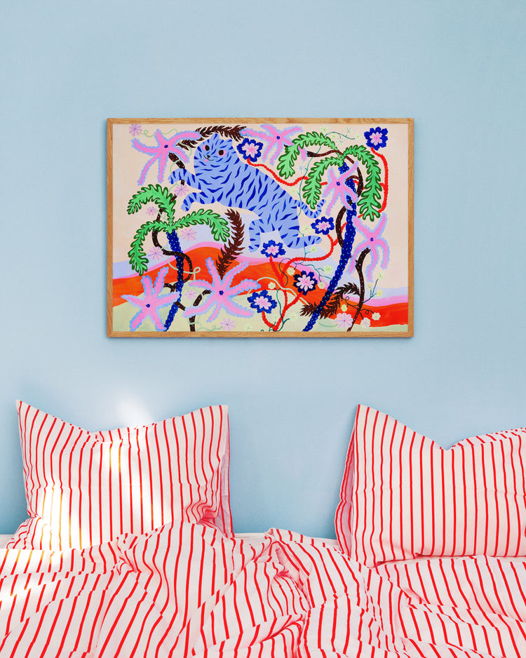 The Dizzy Daizy Poster, a vibrant abstract piece with blue, pink, and red surreal palm tree and flower patterns, adorns a light blue wall. Below it rests a bed dressed with two pillows and a striped red-and-white blanket.