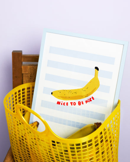 Poster Banana in oak frame laying in a yellow plastic basket filled with bananas