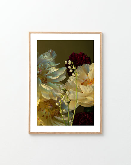 A framed Peony & Lily of the Valley Poster features a still life of white peonies, red carnations, and delicate Lily of the Valley blossoms against a dark background, elegantly displayed on a light-colored wall.