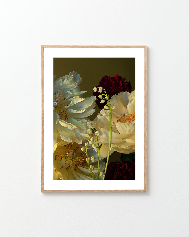 A framed Peony & Lily of the Valley Poster features a still life of white peonies, red carnations, and delicate Lily of the Valley blossoms against a dark background, elegantly displayed on a light-colored wall.