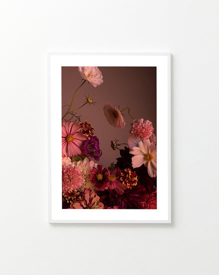 The Dreamscape Poster showcases a framed, vibrant floral arrangement of cosmos and zinnias in pink, red, and purple hues set against a muted brown background. Soft lighting highlights the elegantly arranged flowers and delicate petals.