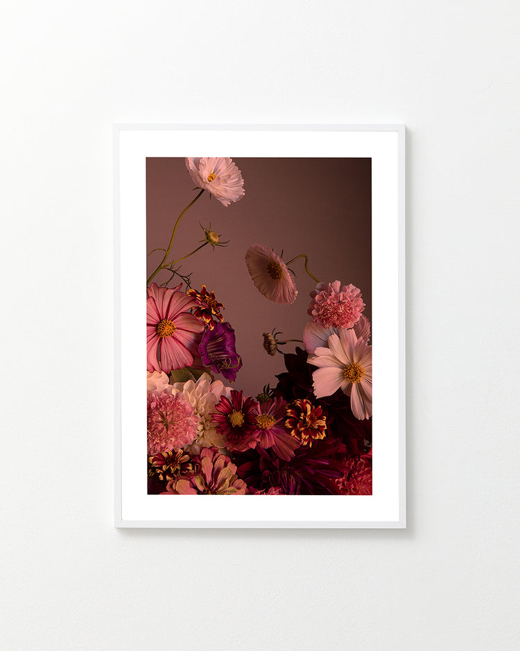 The Dreamscape Poster showcases a framed, vibrant floral arrangement of cosmos and zinnias in pink, red, and purple hues set against a muted brown background. Soft lighting highlights the elegantly arranged flowers and delicate petals.
