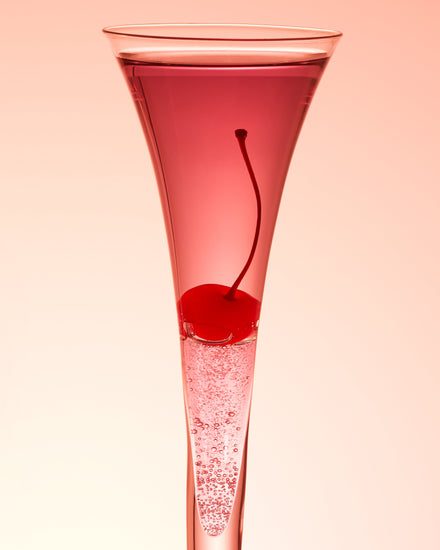 An eye-catching still life photograph showcasing a close-up of a drink adorned with a delectable cherry against a vibrant pink background.