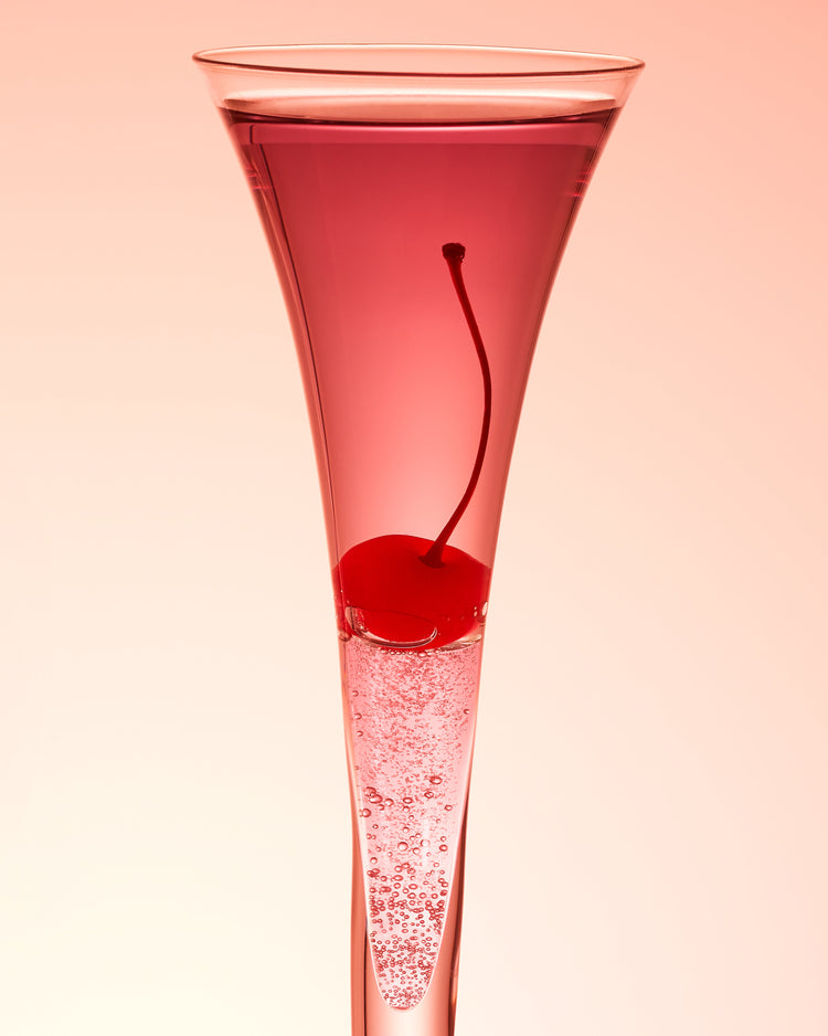 An eye-catching still life photograph showcasing a close-up of a drink adorned with a delectable cherry against a vibrant pink background.