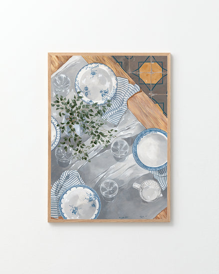 The Good Plates Poster displays a table setting with plates, striped napkins, glasses, and greenery on a white and gray surface. Wooden edges frame the scene, while a tiled corner pattern adds depth and charm.