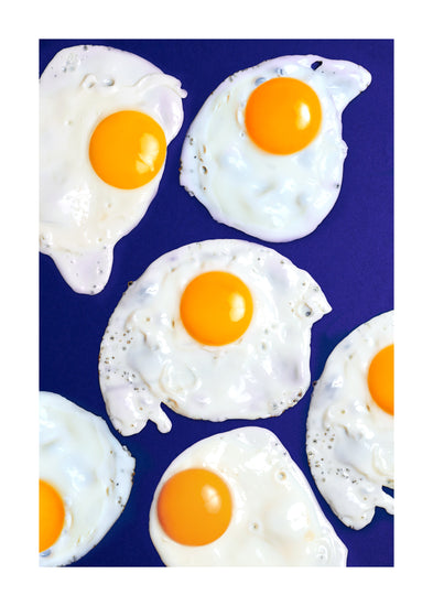 A still life photograph of eggs on a vibrant blue background. White border.