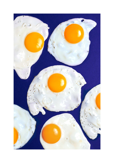 A still life photograph of eggs on a vibrant blue background. White border.