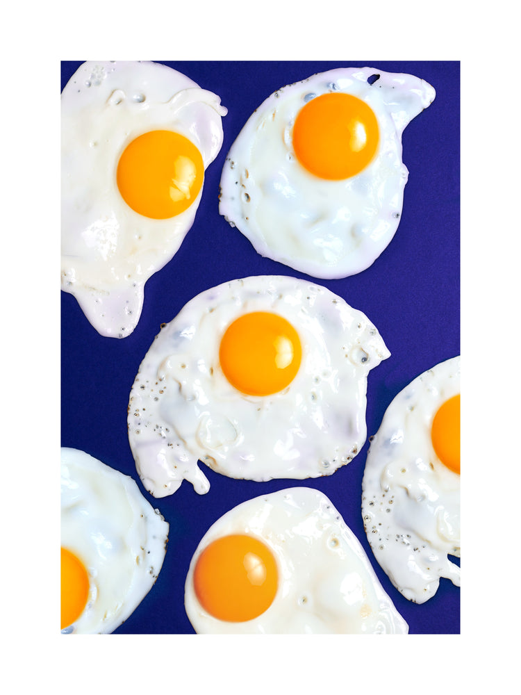 A still life photograph of eggs on a vibrant blue background. White border.