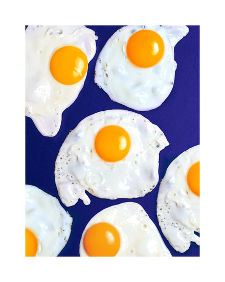 A still life photograph of eggs on a vibrant blue background. White border.