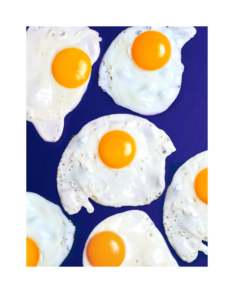 A still life photograph of eggs on a vibrant blue background. White border.