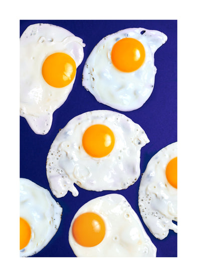 A still life photograph of eggs on a vibrant blue background. White border.