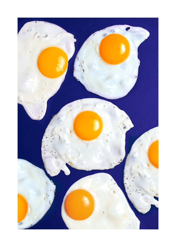 A still life photograph of eggs on a vibrant blue background. White border.