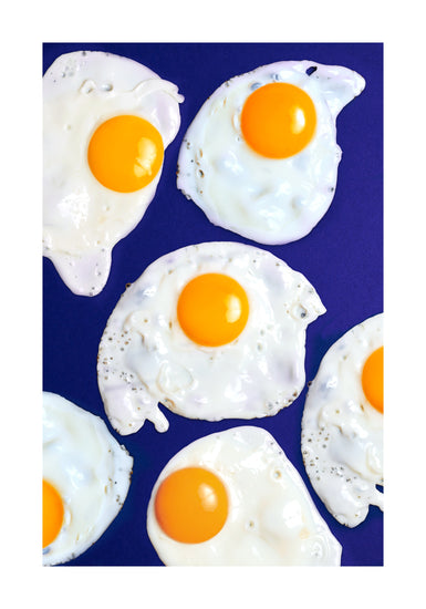 A still life photograph of eggs on a vibrant blue background. White border.