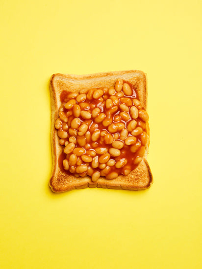 A still life photograph featuring baked beans on toast set against a vibrant yellow background.