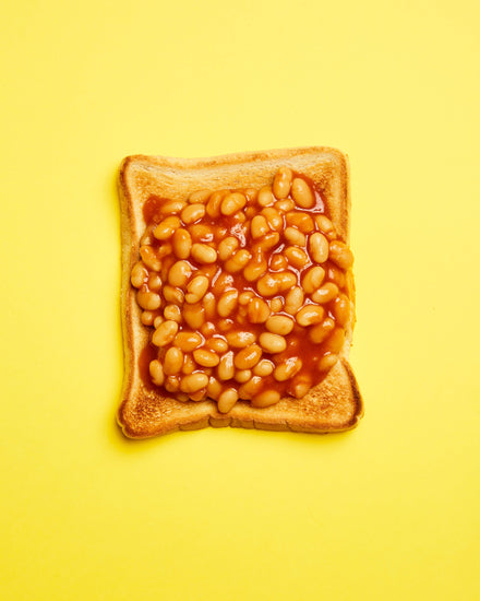 A still life photograph featuring baked beans on toast set against a vibrant yellow background.