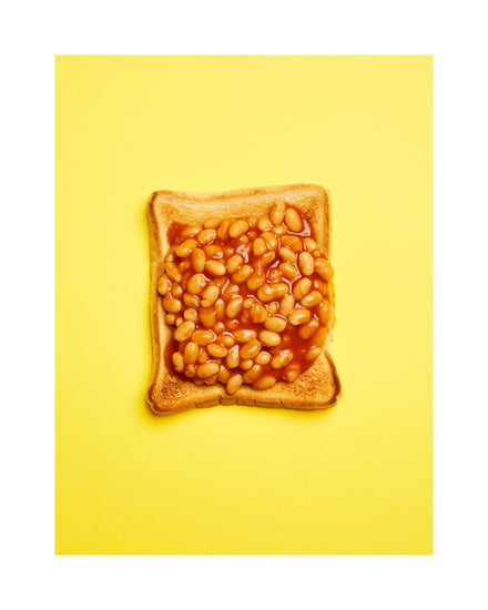 A still life photograph featuring baked beans on toast set against a vibrant yellow background. White border.