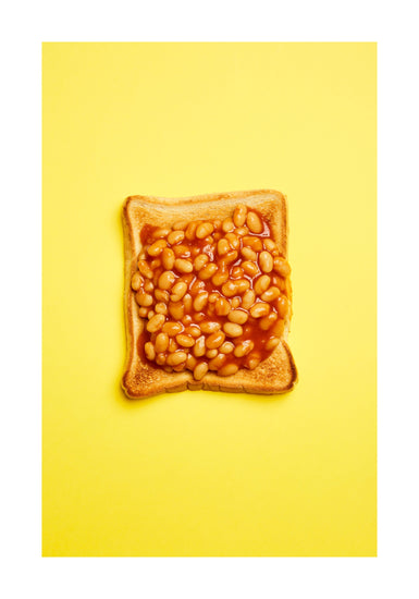 A still life photograph featuring baked beans on toast set against a vibrant yellow background. White border.