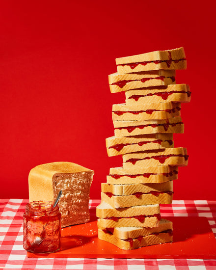 A tower of sandwiches and an empty jam jar on a red and white picnic cloth against a vibrant red backdrop
