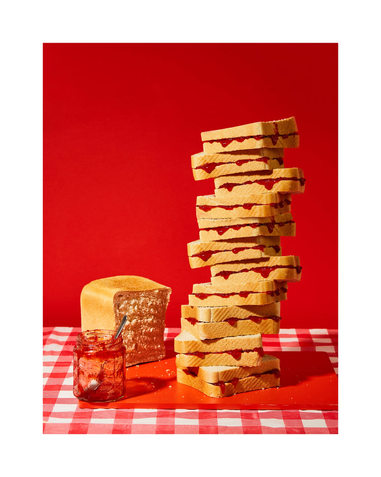 A tower of sandwiches and an empty jam jar on a red and white picnic cloth against a vibrant red backdrop