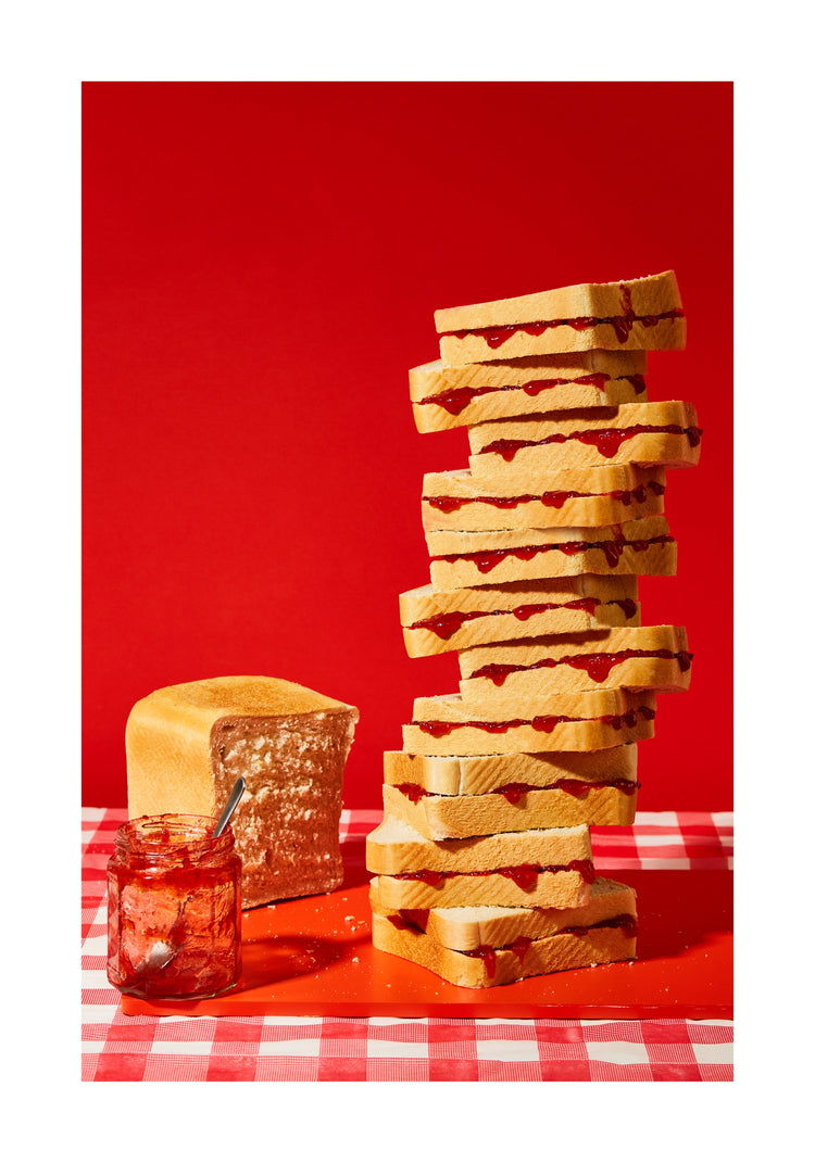 A tower of sandwiches and an empty jam jar on a red and white picnic cloth against a vibrant red backdrop