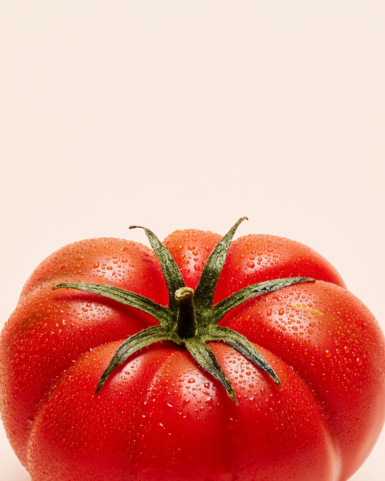 A close-up photograph features a vibrant red tomato adorned with delicate water droplets set against a clean white backdrop.