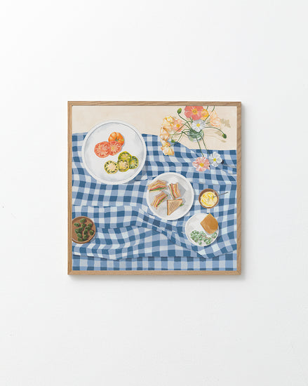 The Poppies and Picnics Poster captures the essence of a summer romance with a blue and white checkered tablecloth, sliced tomatoes, sandwiches, cookies, and a vase of flowers. Its ideal for adding warmth to any kitchen wall against its plain white background.
