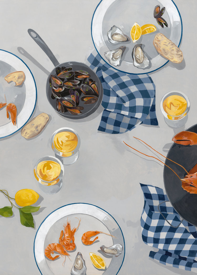 A table set with seafood dishes—oysters, shrimp, and mussels in a pan—served with lemon wedges and bread. Blue checkered napkins match the hues of a nearby Break Out of the Shell I poster. Glasses with yellow drinks glisten on plates set across the light gray surface.