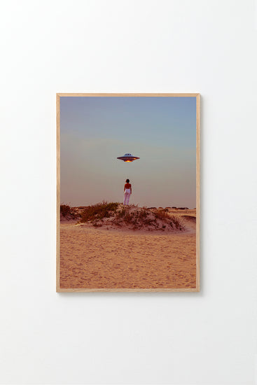 The Hey Luke, our Uber is Here! poster shows a person on a sandy desert dune at sunset, taking a self-portrait while looking at a hovering UFO. Vegetation dots the ground as the sky shifts from blue to orange.