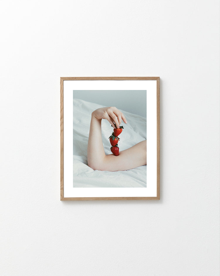 Female arm resting on a sheet with three strawberries stacked on her skin.