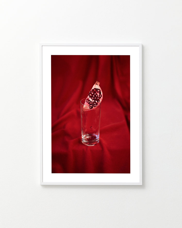 Slice of pomegranate in a glass standing on a blood red sheet.