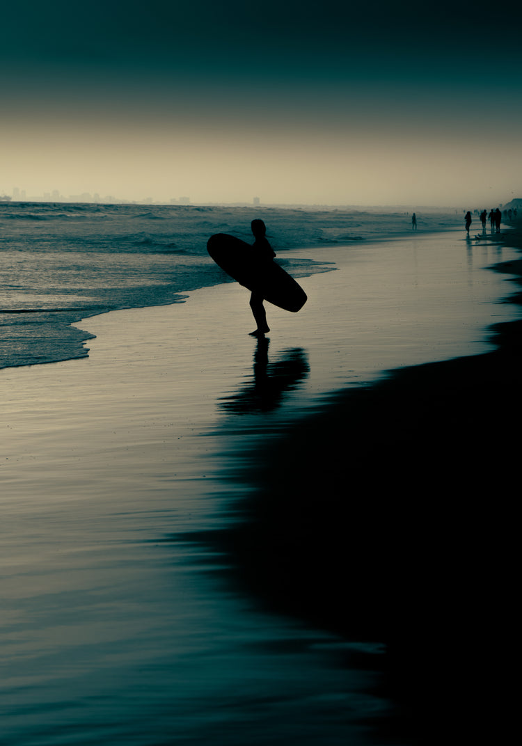 Surfer standing on the shore during low tide under a darkening sky.
