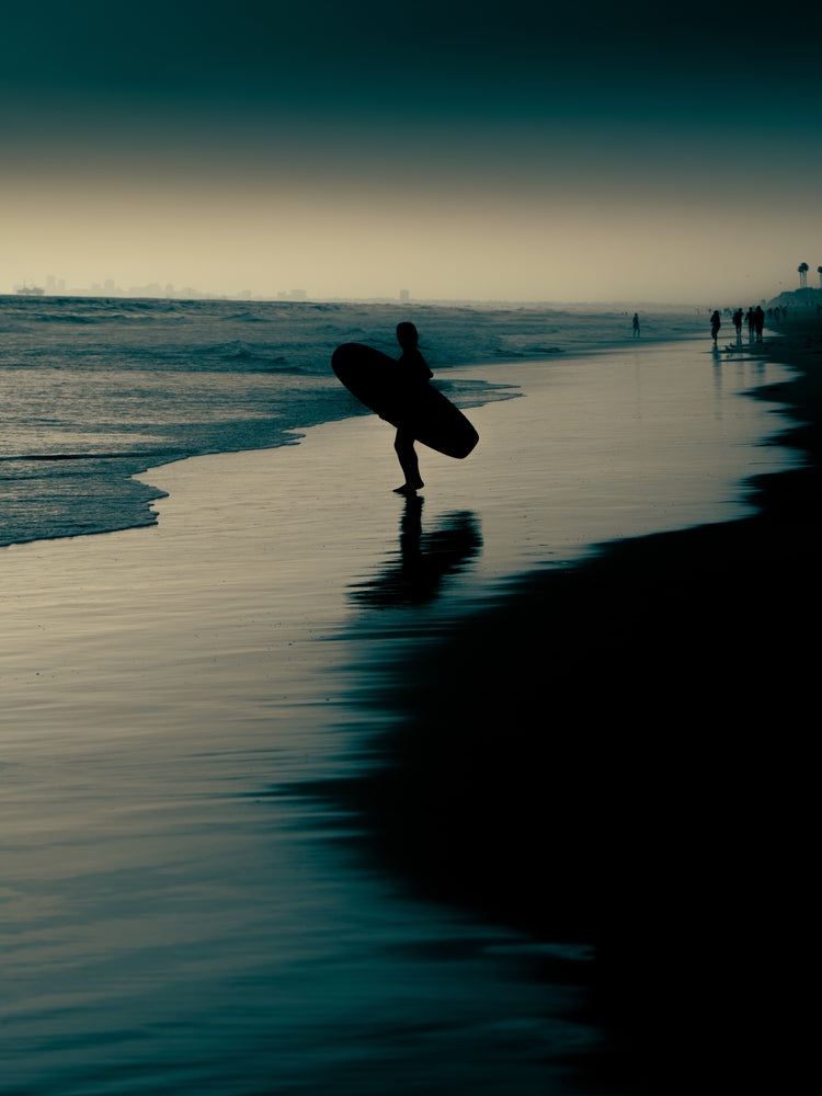 Surfer standing on the shore during low tide under a darkening sky.