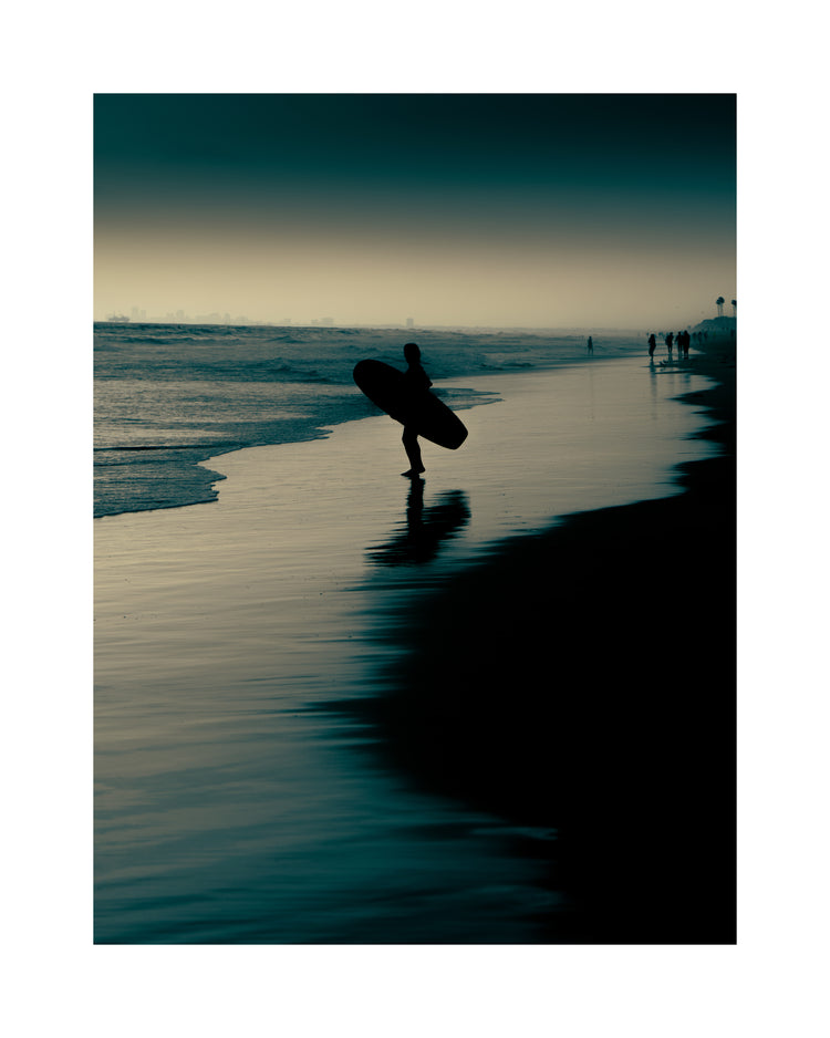 Surfer standing on the shore during low tide under a darkening sky.
