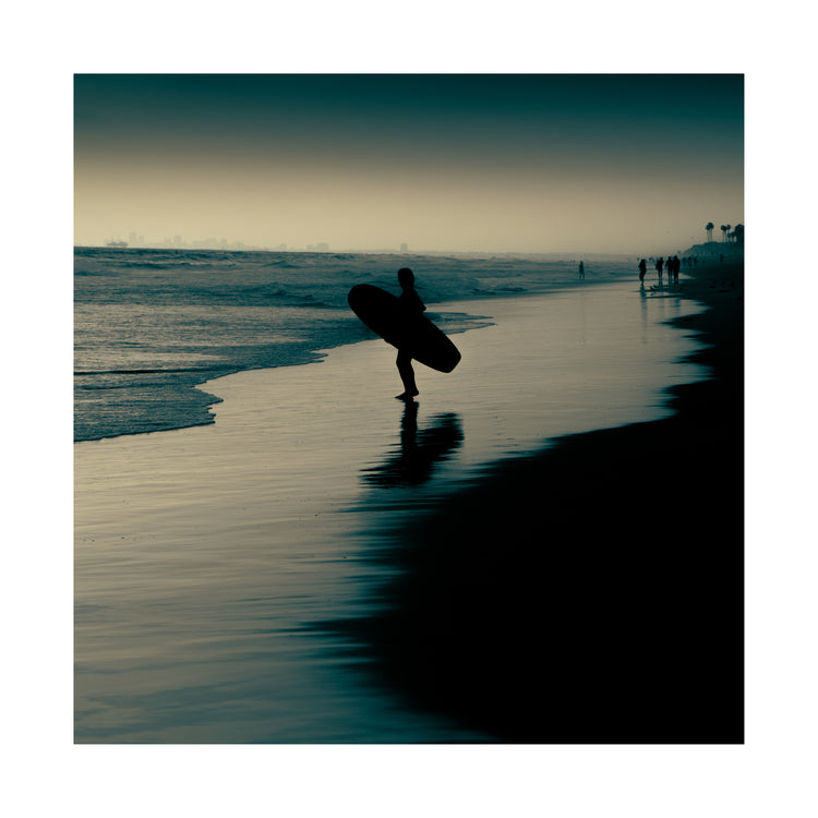 Surfer standing on the shore during low tide under a darkening sky.