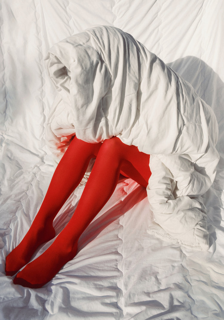 Woman in bright red stockings covered in a thick white down blanket.