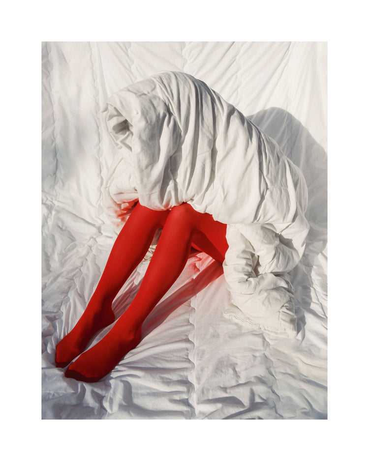 Woman in bright red stockings covered in a thick white down blanket.