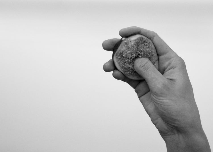 A hand holding half a fig and squeezing its flesh.
