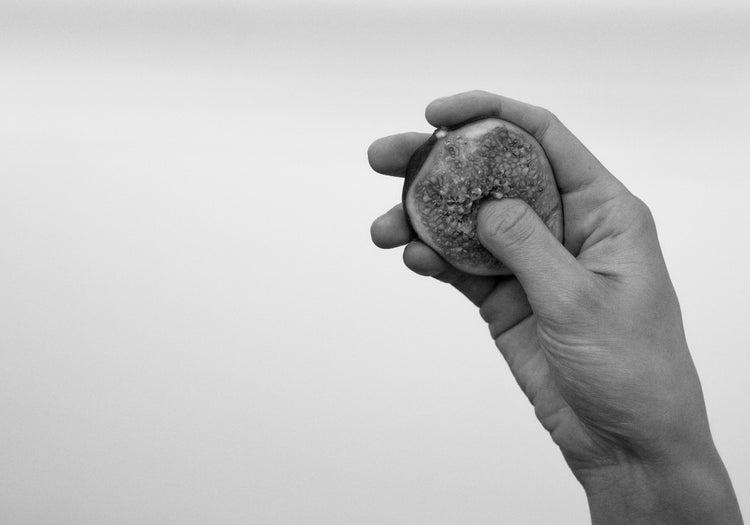 A hand holding half a fig and squeezing its flesh.