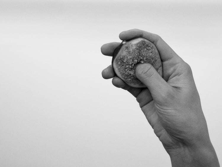 A hand holding half a fig and squeezing its flesh.