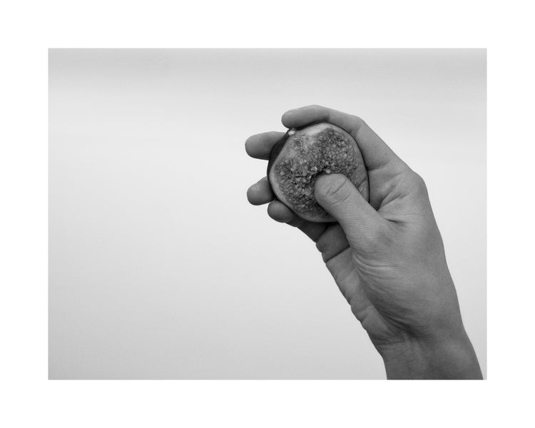 A hand holding half a fig and squeezing its flesh.