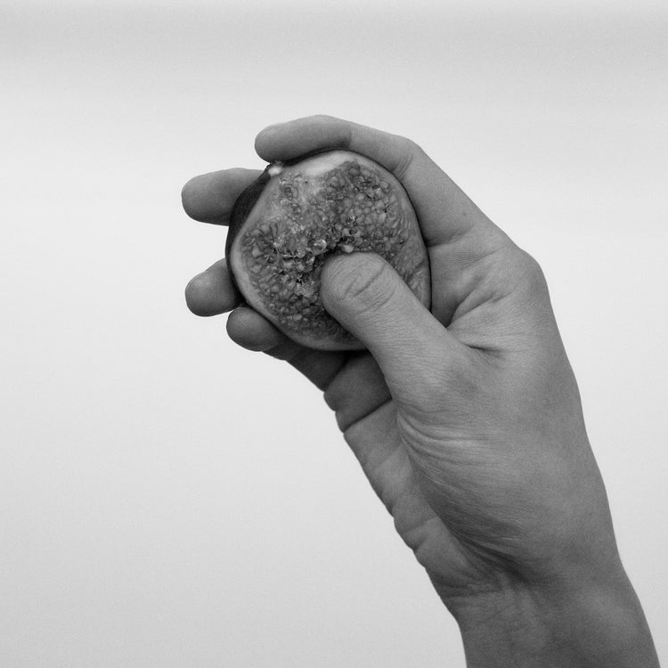 A hand holding half a fig and squeezing its flesh.