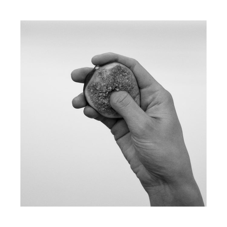 A hand holding half a fig and squeezing its flesh.