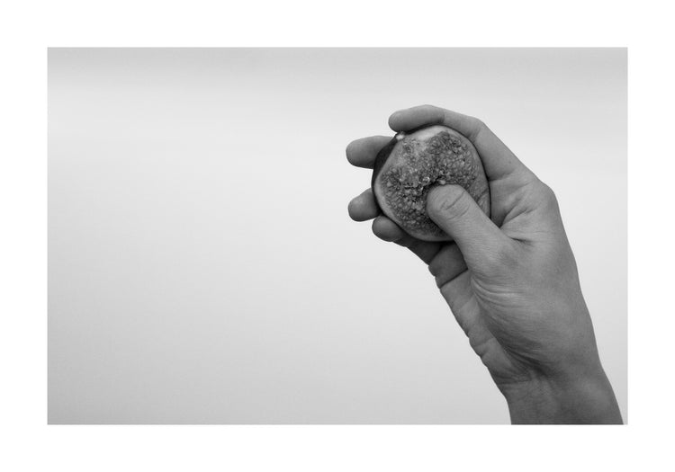 A hand holding half a fig and squeezing its flesh.
