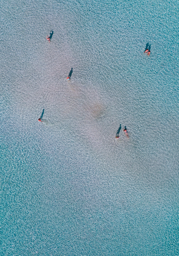 Drone footage of shallow blue waters and people swimming in it.