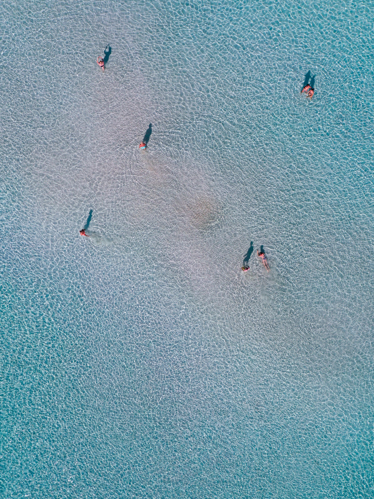 Drone footage of shallow blue waters and people swimming in it.